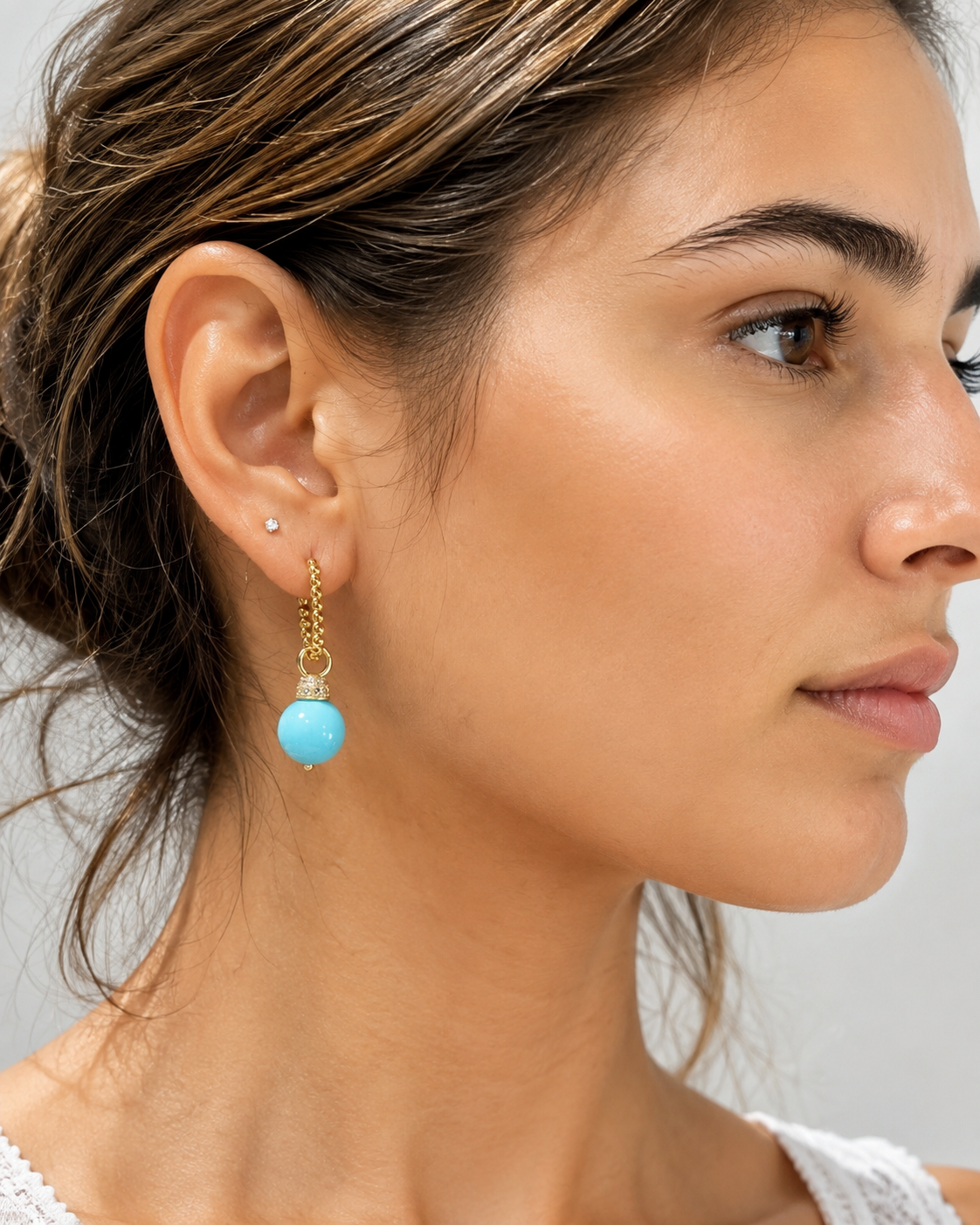 Orecchini pendenti turchese con dettagli in argento 925 dorato e zirconi indossati da modella giovane.