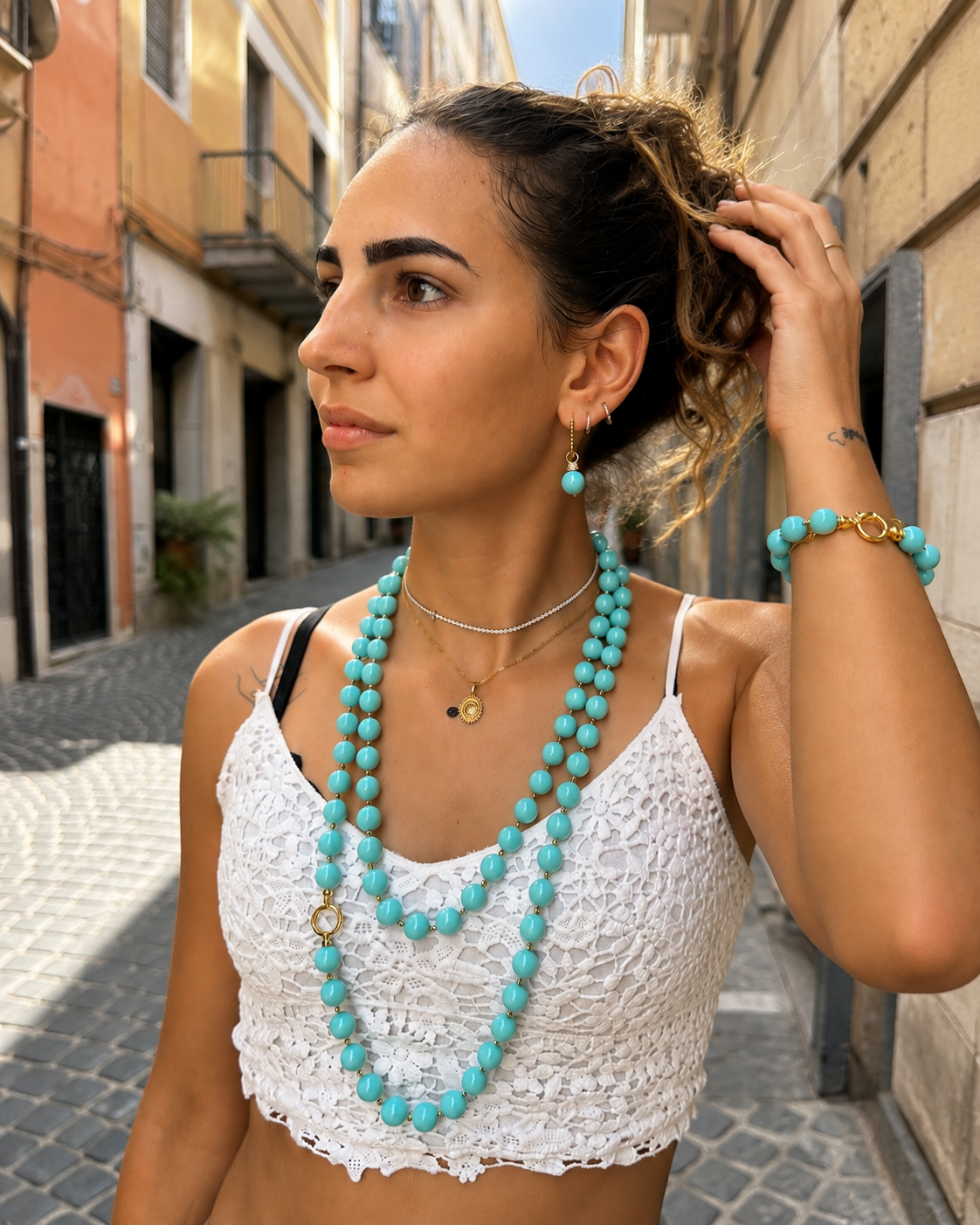Parure con collana, bracciale e orecchini turchese con dettagli dorati indossata da modella giovane.
