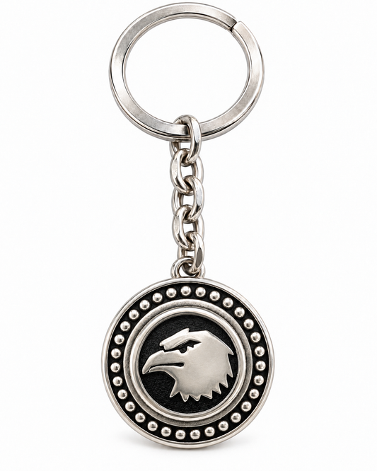 Portachiavi in acciaio inox con medaglione rotondo, aquila color argento su fondo nero, catena a maglie e anello, su sfondo bianco.