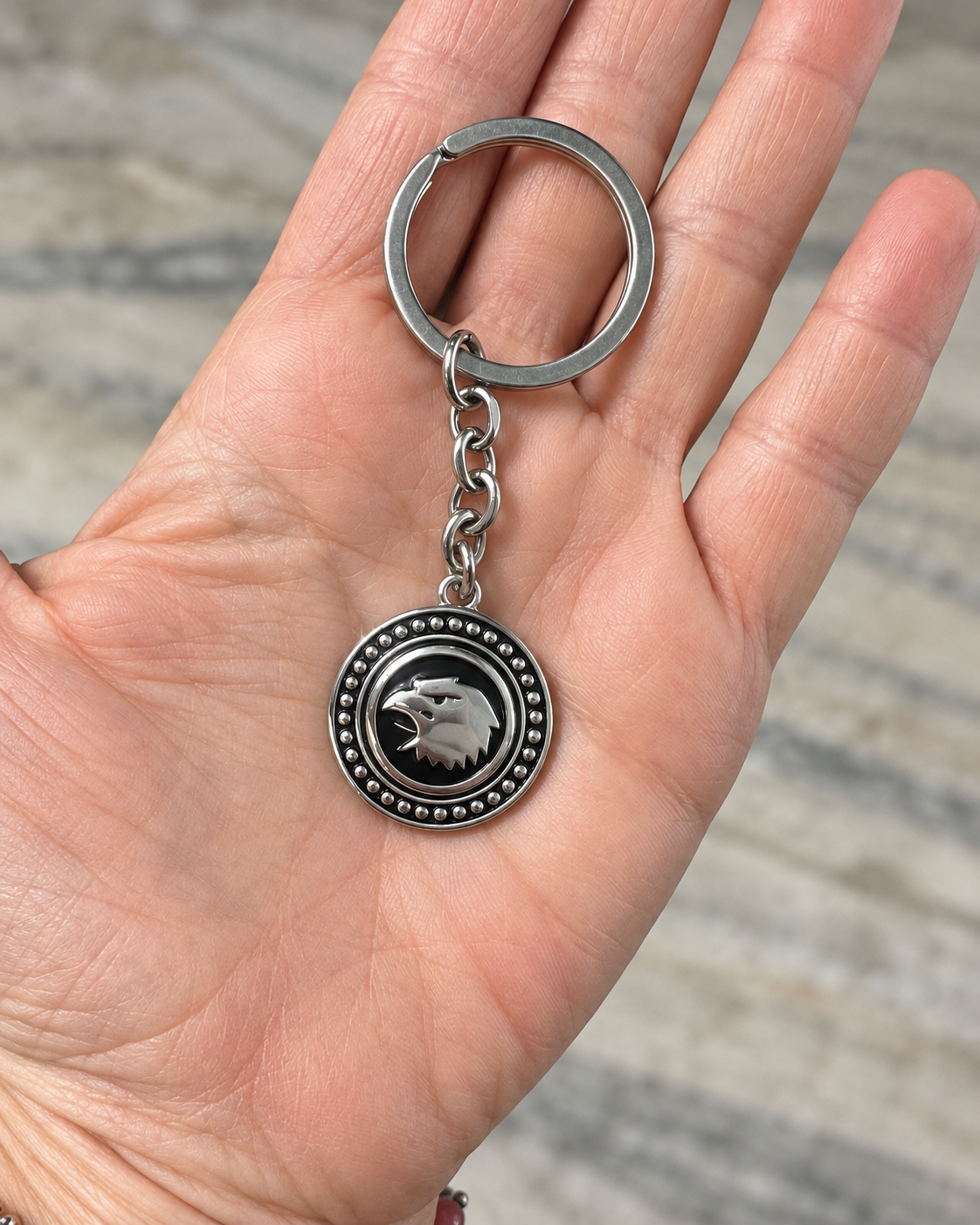 Portachiavi Aquila in acciaio inox appoggiato sul palmo della mano per mostrarne le dimensioni e le proporzioni, con anello, catena e medaglione rotondo.